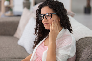 Woman with glasses sitting on couch rubbing jaw