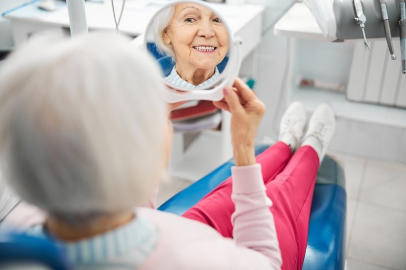An older woman checking her teeth while sitting in a dentist’s chair